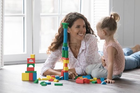 Photo for Beautiful loving mother play wooden cubes with cute little daughter, spend time on warm floor enjoy playtime, family leisure and developmental games at cozy home. Babysitting, upbringing, motherhood - Royalty Free Image