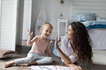 Photo for Mother and daughter drawing pictures giving high five at home. Caring babysitter spend time with preschooler girl, create pictures, finish painting clap hands. Daycare, offspring development, hobby - Royalty Free Image