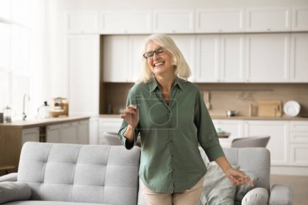 Photo for Joyful excited blonde senior woman in glasses enjoying motion, music, party, dancing in living room with closed eyes, laughing. Retired dancer lady relaxing in home interior - Royalty Free Image