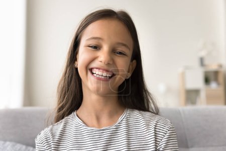Photo for Happy cute pre teen kid girl looking at camera with toothy smile, talking on online video call, chatting on Internet, enjoying distant communication. Home head shot portrait of cheerful child - Royalty Free Image