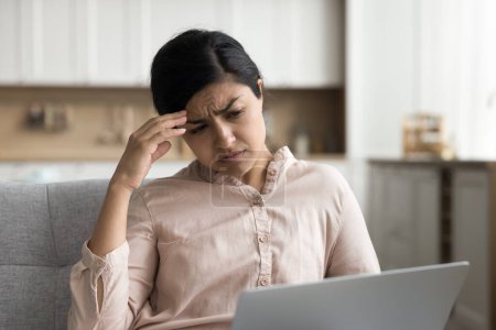 Photo for Concerned tired Indian remote employee woman using laptop computer on home couch, looking at screen, display with worried frustrated face, getting bad news, problems, technologies failure - Royalty Free Image