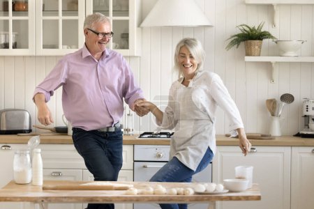 Photo for Happy joyful older husband and mature wife dancing to music in home kitchen, having fun at floury table, baking homemade pastry meal, cooking dessert, keeping active lifestyle - Royalty Free Image