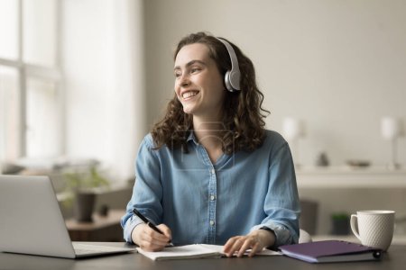 Photo for Cheerful dreamy online college girl in earphones enjoying distant education, studying at laptop, writing notes, looking away, thinking on creative idea for learning project, smiling, laughing - Royalty Free Image