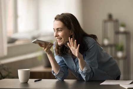 Photo for Happy inspired gen Z young freelancer girl discussing creative idea for business project in mobile phone, talking on speaker, holding smartphone at mouth, smiling, laughing, speaking - Royalty Free Image