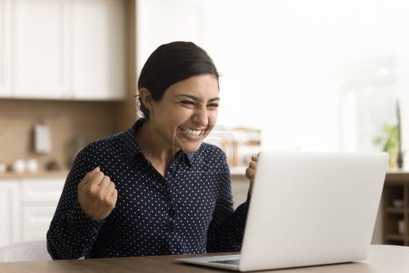 Photo for Happy excited young Indian woman celebrating achievement, triumph, win at laptop display, making winner hands, yes fists, screaming for joy, laughing, having fun, enjoying success, fortune, luck - Royalty Free Image