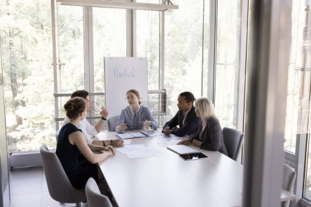 Photo for Business team of diverse colleagues meeting in boardroom with mentor, teacher for corporate training, educating seminar, sitting at table in modern office interior with glass walls - Royalty Free Image