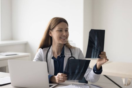 Photo for Happy pretty doctor woman looking at radiography shots of radio bones, smiling, feeling satisfied. Practitioner studying transparent xray scan for diagnosis, medical examining result - Royalty Free Image