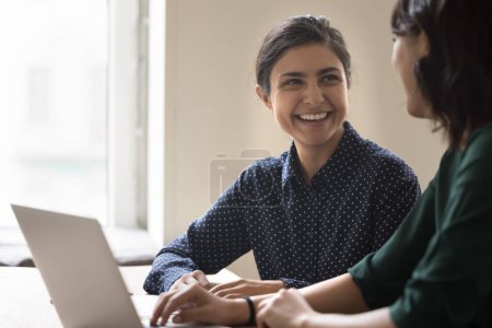 Foto de Feliz joven empleada india hablando con su colega, sonriendo, riendo, discutiendo el éxito de la carrera, la contratación, el trabajo lograr. Mentor y pasante disfrutando de entrenamiento para tareas - Imagen libre de derechos
