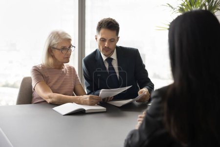 Photo for HR team reviewing paper resume of job candidate, sitting at table. Younger and older employer colleagues talking to applicant woman for hiring, reading work experience list - Royalty Free Image