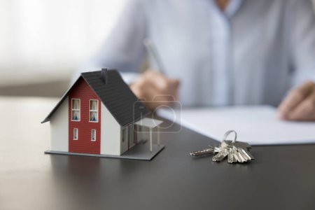 Photo for Female property buyer sign contract, make deal, accept agreement, take bank mortgage for home purchase, close up view to keys and small miniature of cottage house on desk. Real-estate selling services - Royalty Free Image