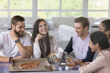 Photo for Happy joyful young friends having fun in pizzeria, meeting and talking in cafe, sitting at table with pizza in box, transparent dish, hot tea, speaking, laughing, enjoying friendship, celebrating - Royalty Free Image