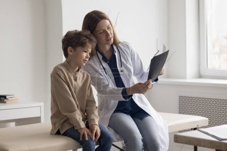 Photo for Focused caring family doctor woman and patient kid watching Xray scan, shot of bones, radiography screening films. Boy visiting pediatrician for medical checkup, diagnosing trauma, illness - Royalty Free Image