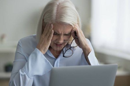 Photo for Close up woman sit near laptop take off glasses suffers from migraine, severe headache due to information overload, experiencing symptoms of eyestrain, blurry vision, feel stressed. Pressure, deadline - Royalty Free Image
