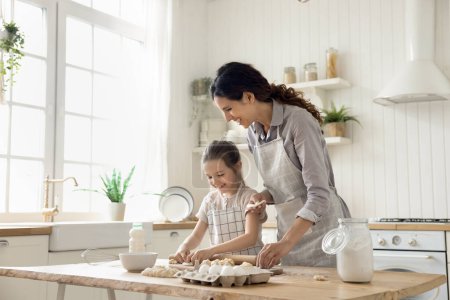 Photo for Hispanic woman teach little daughter to cook, prepare homemade dough for pastries, make holiday pie or cookies on weekend leisure in kitchen at home. Natural products, healthy eating, kid development - Royalty Free Image