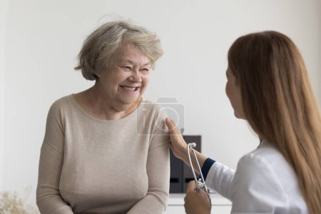 Photo for Positive happy retired older lady visiting doctor, consulting practitioner in office, smiling, laughing. Empathetic physician woman patting shoulder of senior patient, calming old lady - Royalty Free Image