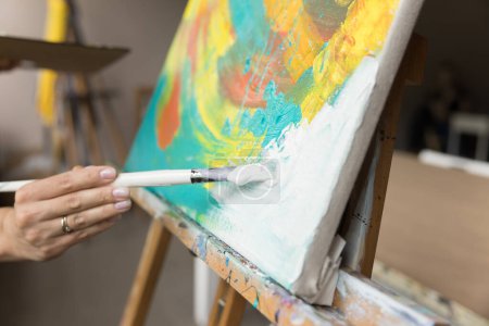 Foto de Artista femenina acariciando blanco sobre lienzo, dibujo abstracto cuadro colorido en pinturas acrílicas, disfrutando de pasatiempo artesanal creativo, estudiando en el estudio de la escuela artística. Tiro recortado de pincel de mano - Imagen libre de derechos