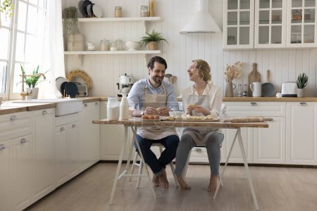 Happy married couple baking together, cooking pastry food, bakery for dessert, festive dinner in home kitchen interior, kneading, shaping dough at floury table, laughing, enjoying domestic hobby