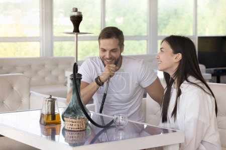 Photo for Happy couple dating in hookah lounge, meeting in tea house, relaxing on couch at table, smoking, drinking, talking, celebrating Valentines day, chatting, laughing, flirting, enjoying leisure - Royalty Free Image
