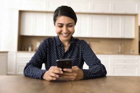 Téléchargez les photos : Joyeux belle femme d'affaires indienne utilisant l'application en ligne sur téléphone mobile, s'amuser, rire, taper sur le gadget numérique, faire un appel vidéo, profiter de la communication Internet - en image libre de droit