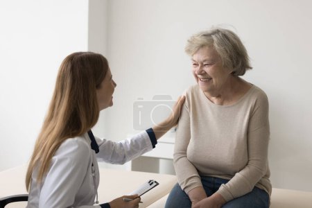 Mujer doctora joven reuniéndose con una paciente anciana mayor, tocando el hombro con cuidado, apoyo, simpatía, calmante, dando consuelo, consejo médico, preguntando sobre quejas de salud