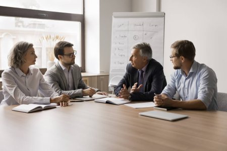 Photo for Serious older businessman speaking to business partners, discussing cooperation, partnership, problem solving, negotiating in office boardroom. Boss talking to employees on meeting - Royalty Free Image