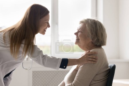 Photo for Cheerful practitioner woman visiting senior 80s female patient, patting shoulder with care, support, sympathy, hope, giving comfort, empathy, asking about health complaints, smiling, laughing - Royalty Free Image