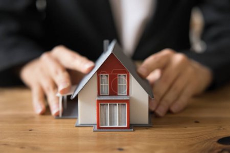 Photo for Hands of real estate, insurance agent touching toy house on work table, promoting rent of apartment. Female realtor, mortgage broker offering loan for property buying. Close up cropped shot - Royalty Free Image