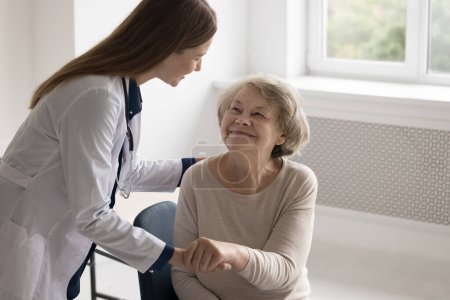 Photo for Positive empathetic doctor woman giving comfort to elderly patient with geriatric diseases, patting back, holding arm, touching hand, expressing support, medical care, speaking, smiling - Royalty Free Image