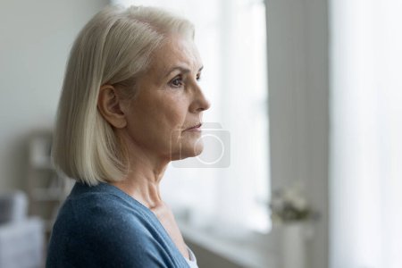 Close up portrait of serious upset older woman looking out window, lost in thoughts, think about problems, remember past, ponder future, feels depressed or lonely. Memories, melancholy, nostalgic mood