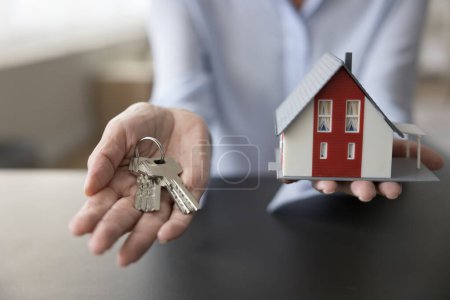 Foto de Unknown mature female hands holding bunch of keys and miniature of modern chalet house, close up. Housing improvement, purchase of new property, real-estate selling and buying services. Bank mortgage - Imagen libre de derechos