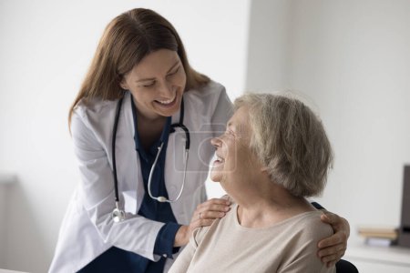 Alegre doctora con estetoscopio tocando hombros de feliz anciana anciana anciana paciente, abrazando a anciana con cuidado, apoyo, hablar, sonreír, reír
