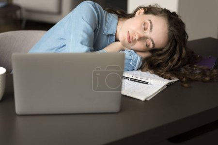 Foto de Muchacha profesional independiente joven agotada que se duerme en el escritorio, colocando la cabeza con los ojos cerrados en la mesa en el ordenador portátil, sintiéndose extremadamente cansado, frente al estrés, burnout, plazo - Imagen libre de derechos