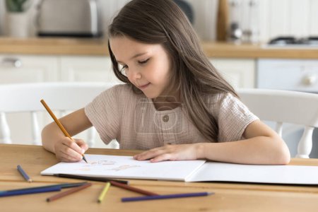 Little girl painting pictures in paper sketchbook with pencils. Cute kid sit at table in cozy domestic kitchen drawing in album, looking focused, enjoy creative activity, favourite hobby alone at home