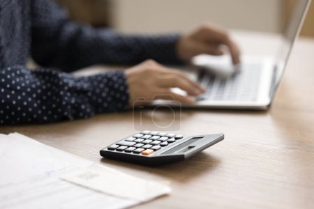 Photo for Calculator on table surface and cropped view of female hands typing on laptop keyboard. Freelancer, accountant woman working at computer, using financial application for job - Royalty Free Image