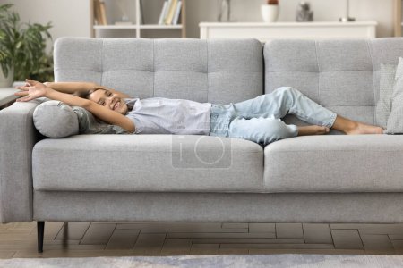 Foto de Niña alegre descansando en un sofá suave en una casa acogedora, estirando el cuerpo, recostado, sonriendo, riendo, disfrutando del ocio, comodidad hogareña, relajándose, respirando aire fresco en el interior - Imagen libre de derechos