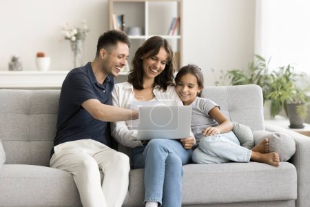 Photo for Happy young parents and cute kid relaxing at laptop on sofa, holding computer on lap, using online media service for watching movie, entertainment, enjoying Internet technology, connection at home - Royalty Free Image