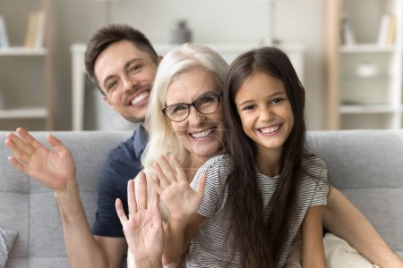 Photo for Cheerful pretty preteen kid girl, happy grandma and young handsome dad looking at camera, waving hand hello, sitting in line behind each other, smiling, laughing, posing for family portrait - Royalty Free Image