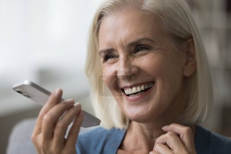 Photo for Close up portrait happy aged woman spend leisure talking on mobile phone, record audio message on cellphone, leave voice mail, use modern app. Remote communication, tech, AI, virtual assistant usage - Royalty Free Image