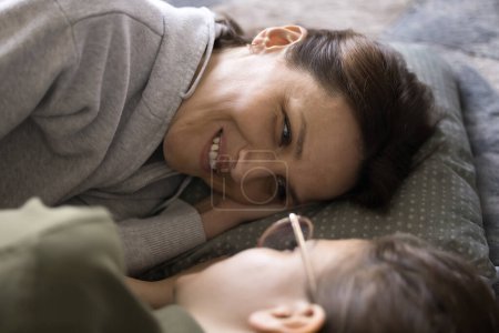 Photo for Happy mom resting in bed, lying on side, talking with teenager daughter child in glasses, enjoying leisure, communication, trustful conversation with kid, looking at girls face, smiling - Royalty Free Image