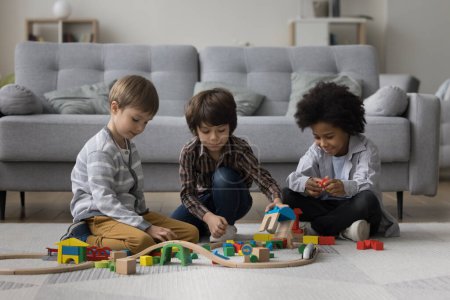 Tres niños preescolares diversos jugando con juguetes en la calefacción alfombrado piso, disfrutando del ocio, tiempo de juego, el desarrollo de juego, la construcción de carreteras de la ciudad de bloques de construcción juntos
