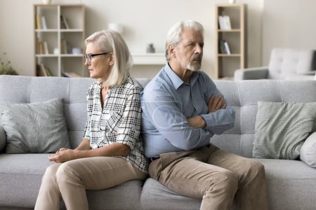 Photo for Annoyed ignoring senior couple sitting on home couch back to back, looking away, keeping silence after arguing, thinking on breakup, separation, relationship problems, conflict - Royalty Free Image
