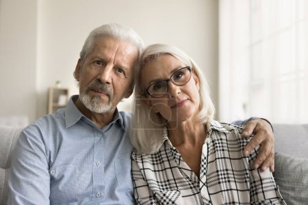 Photo for Serious senior old couple video call screen head shot portrait. Elderly husband and wife hugging on home sofa with care, affection, support, looking at camera, posing for family picture - Royalty Free Image