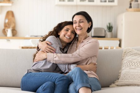 Photo for Two beautiful women, older mother and young millennial daughter embracing relaxing seated on cozy sofa in modern living room, enjoy life moments, feeling unconditional love, appreciate time together - Royalty Free Image