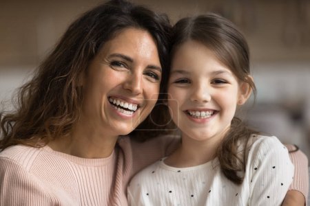 Photo for Positive beautiful mom and happy tween kid girl looking at camera, smiling, showing white healthy teeth, posing for home close up portrait. Cheerful mother and cute daughter head shot - Royalty Free Image