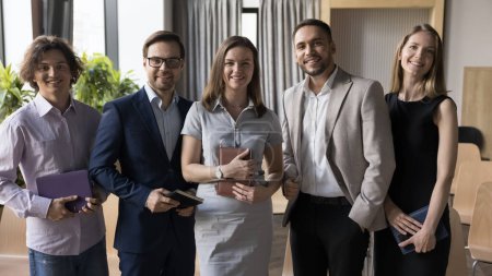 Fünf Profis, eine Gruppe Geschäftsleute, Büroangestellte, die für ein Firmenfoto posieren, lächeln in die Kamera und stehen in einer Reihe in einem modernen Arbeitsraum. Karriere, Aufstieg, Unternehmensförderung und Erfolg