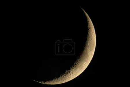Crescent Moon on dark black sky background, shot from surface of earth with very long telephoto lens. Grey white moon glowing at clear sky.