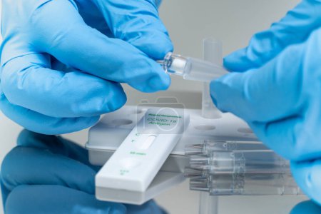 Person in blue gloves performs COVID-19 rapid test at home using personal home test kit for in vitro diagnostic use only.