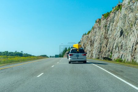 Photo for Travelers car with yellow canoe camping luggage and equipment. Concept of driving to cottage or cabin for holiday in the wilderness woods. Mountains or rocky walls at the road side. Highway. - Royalty Free Image