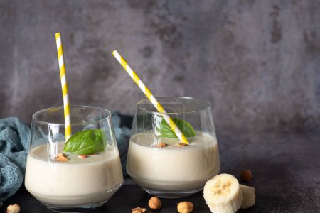 Fresh, healthy smoothie with banana and hazelnuts, in a glass cup with a yellow-white drinking tube