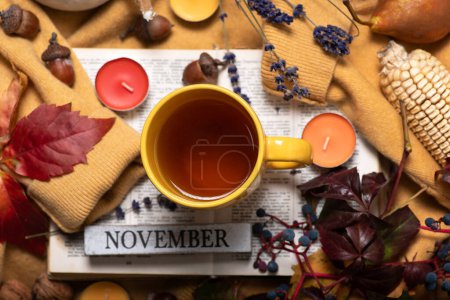 Herbstthema mit Herbstfrüchten und Farben. Ein gelber Pullover mit einer Tasse Tee darauf, ein Buch, Herbstblätter, kleine Duftkerzen und verschiedene Früchte. Monat November abstrakter Hintergrund